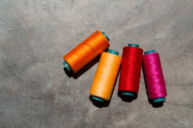 Gri bir yüzeye dört farklı renkli iplik makarası serilmiştir. Renkler turuncu, pembe, kırmızı ve sarıdır. Makarnalar sıraya dizildi, soldaki turuncu olanla.