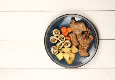 Patatesli fırında ördek, havuç ve hafif ahşap arka planda bir tabakta meyveli bisküvi. Üst manzara, düz uzanma