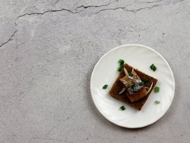 Açık gri arka planda yuvarlak bir tabakta soğanlı tuzlu ringa fileto. Üst manzara, düz uzanma