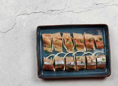 Açık gri arka planda, dikdörtgen bir tabakta soğanlı tuzlu ringa fileto. Üst manzara, düz uzanma