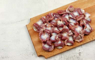 Açık gri arka planda tahta kesme tahtasının üzerinde çiğ tavuk midesi. Üst manzara, düz uzanma