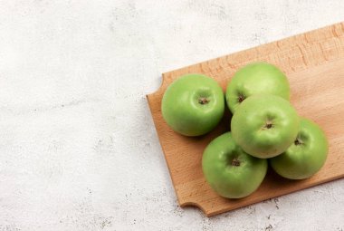 Açık gri arka planda tahta kesme tahtasındaki yeşil elmalar. Üst manzara, düz uzanma