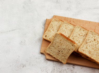 Açık gri arka planda tahta kesme tahtasının üzerinde çoklu tahıllı ekmek dilimleri. Üst manzara, düz uzanma