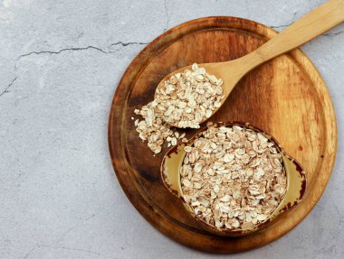 Kasedeki yulaf ezmesi ve açık gri arka plandaki tahta kesme tahtasındaki tahta kaşık.