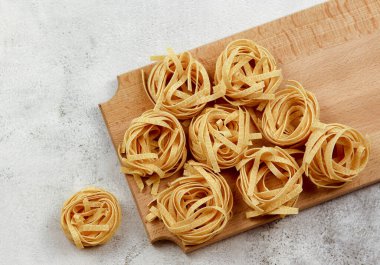 Açık gri arka planda tahta bir kesme tahtasının üzerinde düz, düz şekilli makarna tagliatelle. Üst manzara, düz uzanma