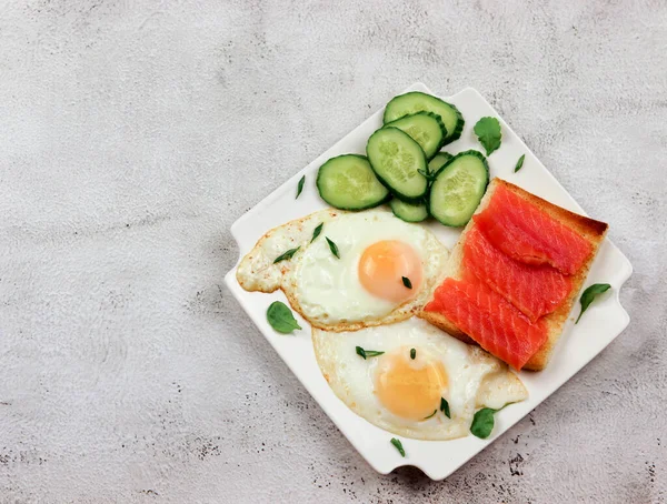 Fried eggs with cucumbers and salted salmon on a white rectangular plate on a light gray background. Top view, flat lay — Stock Image Fried Eggs Cucumbers Salted Salmon White Rectangular Plate Light Gray Stock Image