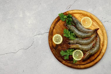 Çiğ karidesler ahşap bir zeminde, tahta bir tahtanın üzerinde servis edilir. Üst manzara, düz uzanma