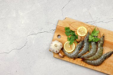 Çiğ karidesler ahşap bir zeminde, tahta bir tahtanın üzerinde servis edilir. Üst manzara, düz uzanma