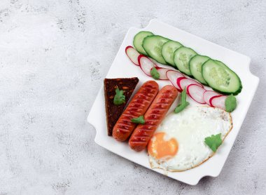 Yağda yumurta, sosis, dilimlenmiş sebze ve açık gri arka planda beyaz dikdörtgen bir tabakta tost. Üst manzara, düz uzanma