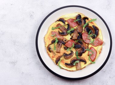 Açık gri arka planda yuvarlak tabakta mantarlı, peynirli ve sosisli omlet. Üst manzara, düz uzanma