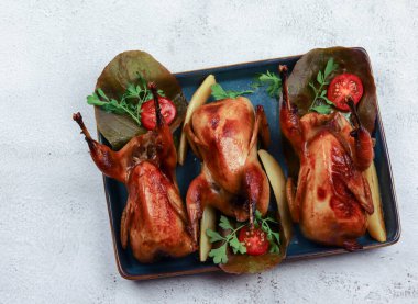 Açık gri arka planda kare bir tabakta pişirilmiş bıldırcın. Üst manzara, düz uzanma