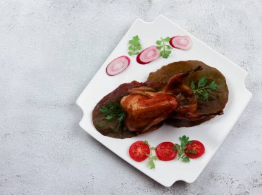 Açık gri arka planda kare bir tabakta pişirilmiş bıldırcın. Üst manzara, düz uzanma