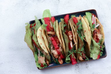 Yeşil salatalı taco, biber, açık gri arka planda kare tabakta tavuk. Üst manzara, düz uzanma