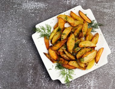 Siyah arka planda beyaz dikdörtgen bir tabakta otlu kızarmış patates. Üst manzara, düz uzanma