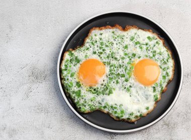 Açık gri arka planda yuvarlak tabakta yeşil soğanlı sahanda yumurta. Üst manzara, düz uzanma