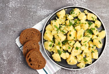 Siyah arka planda yuvarlak tabakta maydanozlu haşlanmış patates. Üst manzara, düz uzanma