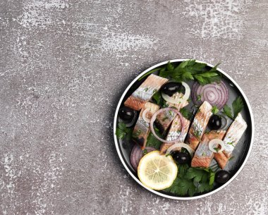 Siyah arka planda yuvarlak tabakta soğanlı, zeytinli ve otlu ringa filetosu. Üst manzara, düz uzanma