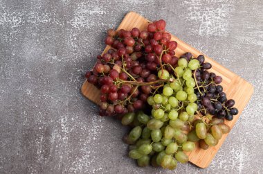 Koyu arkaplanda tahta kesen dikdörtgen üzerinde çeşitli olgun üzümler. Üst manzara, düz uzanma