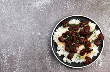 Koyu arkaplanda yuvarlak tabakta pirinçli kırmızı domuz eti. Üst manzara, düz uzanma