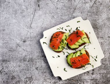 Kare tabakta koyu bir arka planda somon ve avokado sandviçi. Üst manzara, düz uzanma