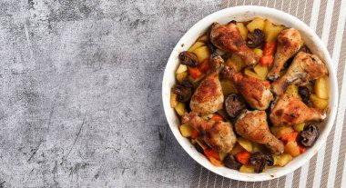 Koyu arkaplanda beyaz bir kabın içinde patatesli tavuk budu. Üst manzara, düz uzanma