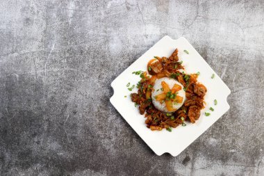 Kare bir tabakta kaynamış pirinçli tavuk taşları ve koyu gri bir arka plan. Üst manzara, düz uzanma