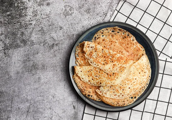 Traditional russian yeast thin pancakes (crepes) on a round plate on a dark gray background. Top view, flat lay