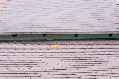 Orange frisbee forgotten on brown asphalt roof clipart