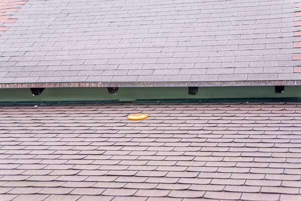 Orange frisbee forgotten on brown asphalt roof