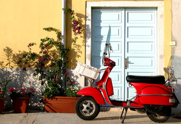 An red old-fasioned retro scooter parked in front of  door in a street in italy. - concept of vintage style of transport veicle