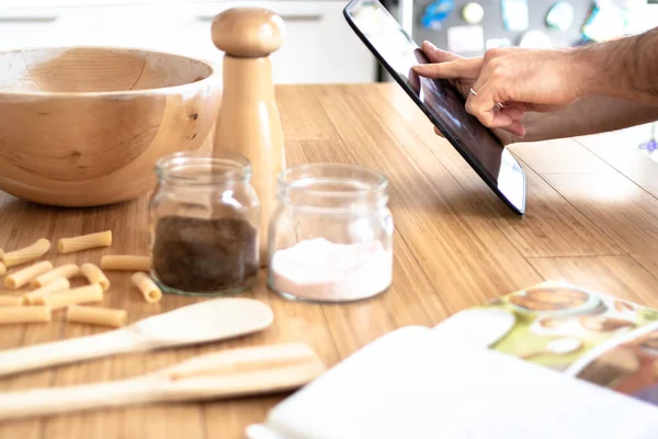 man preparing food in the kitchen reading from the web with tablet an online cooking recipe, with her finger on the tablet, cookbook on the wooden kitchen table. modern woman cooking - only hands