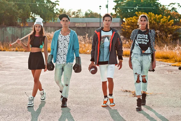 A portrait of an interracial group of 4 young adults walking on and old parking lot in front of an old, vacant graffiti sprayed store front during a pleasant summer day wearing sportive urban outfits.