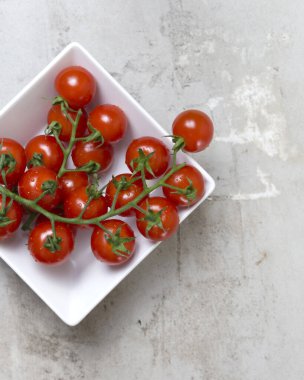 Kırmızı küçük domates dalıyla kirazlı beyaz kare kasede gri beton arka planda. Düz yatıyordu 