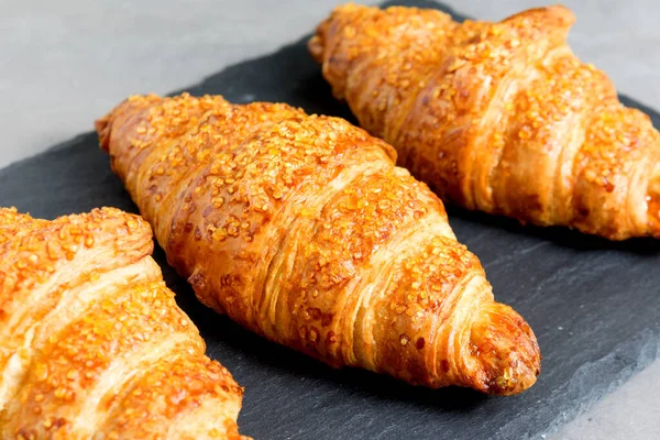 Tres sabrosos croissants sobre fondo de piedra negra. Comida francesa. De cerca. Tecla baja — Foto de Stock