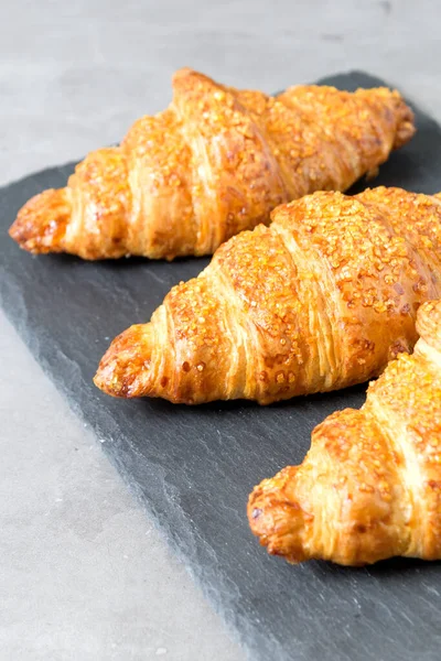 Tres sabrosos croissants sobre fondo de piedra negra. Comida francesa. De cerca. Tecla baja — Foto de Stock