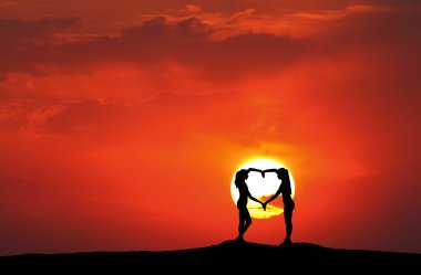 Genç sportif Kadınlar Elele kalp şeklinde günbatımında