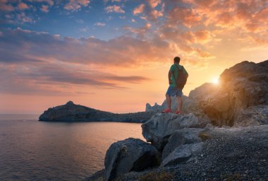 Young standing man with backpack on the stone at sunset
