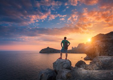 Young standing man with backpack on the stone at sunset