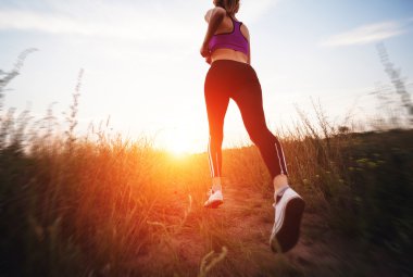 Young woman running on a rural road at sunset 