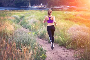 Young woman running on a rural road at sunset 