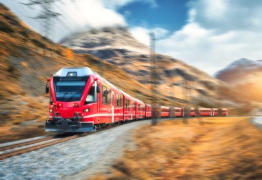 Kızıl modern yolcu treni sonbaharda günbatımında İsviçre Alplerinde demiryolunda hareket ediyor. Dağlarda, yolda yüksek hız treni hareket bulanıklığı ile sonbaharda portakal ağaçları. Bernina Ekspresi, İsviçre