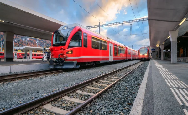 Sonbaharda İsviçre Alpleri 'ndeki dağ tren istasyonunda modern kırmızı yolcu treni. Hızlı tren, demiryolu platformu ve bulutlu gökyüzü. Bernina Ekspresi. Demiryolu taşımacılığı. St. Moritz, İsviçre 'deki istasyon.