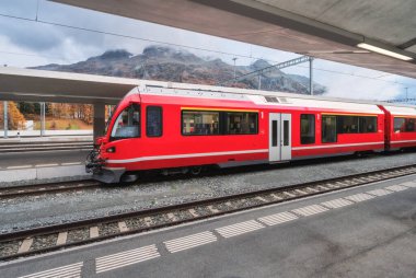 Sonbaharda İsviçre Alpleri 'ndeki dağ tren istasyonunda modern kırmızı yolcu treni. Hızlı tren, demiryolu platformu ve bulutlu gökyüzü. Bernina Ekspresi. Demiryolu taşımacılığı. St. Moritz, İsviçre 'deki istasyon.