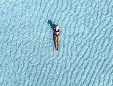 Mavi bikinili, beyaz şapkalı, turkuaz açık denizde kum dalgalarıyla uzanan sportif kadın görüntüsü. Zanzibar 'da tropik bir yaz tatili. Sıska kızın en iyi drone görüntüsü, okyanus berrak su, kum