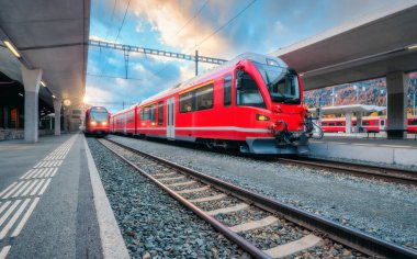 Sonbaharda İsviçre Alpleri 'ndeki dağ tren istasyonunda günbatımında kırmızı modern yolcu treni. Yüksek hızlı tren, demiryolu platformu ve mavi gökyüzü. Bernina Ekspresi. St. Moritz, İsviçre 'deki tren istasyonu.