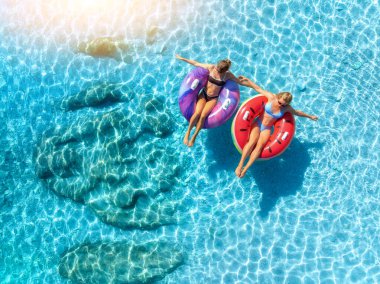Mavi denizde yüzen iki güzel genç kadının hava manzarası. Yaz tatili. Açık turkuaz suda şişme halkalar üzerinde yüzen sportif kızların en iyi drone görüntüsü. Adriyatik Denizi, Hırvatistan