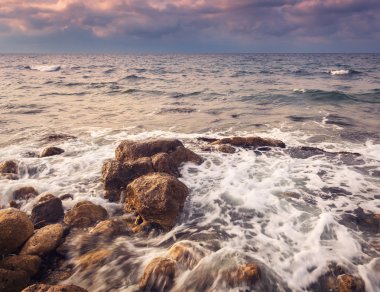 Gün batımında sahilde taşlarla dalgalar deniz