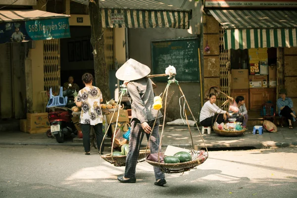 Woman vendor carrying baskets with fruits on the street of Hanoi — Stock Photo, Image