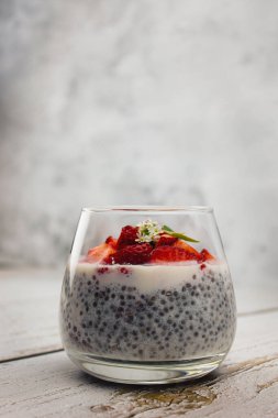 Laktozsuz sütten yapılmış tatlı, yanında Chia tohumları ve gri arka planda bir bardakta çilek. Temiz yemek, detoks, kilo verme konsepti. Düşük karbonhidratlı diyet tarifi..