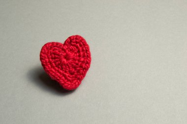 Gri arkaplandaki kırmızı ipliklerden yapılmış bir kalp. Kalp büyük değildir.